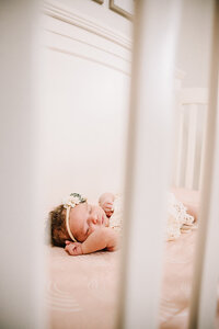 A newborn baby sleeps in her crib. This picture looks at her through the crib arms.