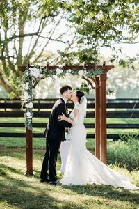 Couple kissing beneath a wooden arbor during an outdoor ceremony at Bradshaw Duncan House, a popular wedding venue near Louisville.