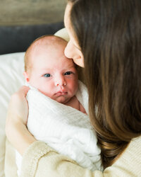 Mother kissing her newborn baby’s forehead during a natural in-home lifestyle newborn session.