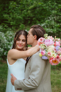 Groom kissing bride as she holds a peony bouquet designed by Flowergirl Cville. Photography by Jessa Rose Moments.