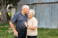 Elderly couple sharing a sweet candid moment outdoors near a rustic building, natural lifestyle portrait captured by Kaitlyn Dawn Photography, extended family photographer.