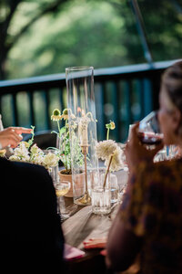 A guest sipping wine gazes at a beautifully decorated outdoor dinner table, featuring flowers, glowing candles, and glassware.