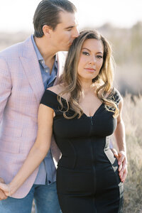 Romantic portrait of a couple from the Parker family in Las Vegas, with the man gently kissing the woman’s head as they stand together in soft golden light during an outdoor desert session.