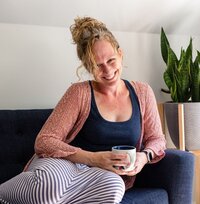 Kelly Loss holds a tea cup while smiling on a blue sofa