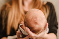 A soft baby head with a swirl of hair lies in his mother's hands. The mom is out of focus in the background.