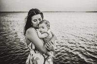 A mother embraces her infant son while at a lakeside photo session.