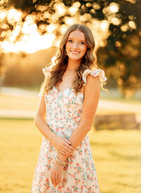 Senior portrait in downtown Magnolia Springs, Alabama — holding her left wrist gently while smiling.