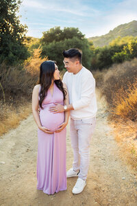 expecting couple holding baby bump during outdoor emotional maternity portrait session in Franklin Canyon Park