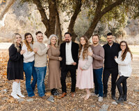 Large extended family standing together outdoors under tall trees with warm fall tones, natural light portrait by Kaitlyn Dawn Photography, professional extended family photographer specializing in timeless group portraits.
