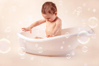 one year old splashing water in small studio tub during birthday session