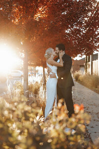 a newlywed couple kissing under fall colored trees.