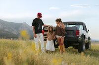 A family smile in an open meadow in front of a vintage truck & with mountain backdrop during family photography session near Boulder Colorado.