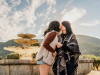 Same sex couple during a surprise proposal in a Temecula Valley vineyard, with a fountain in the background as one partner prepares to propose.