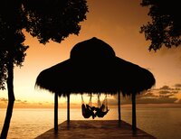 Candlelit beachfront dinner under a thatched hut at sunset, perfect for luxury romantic escapes.