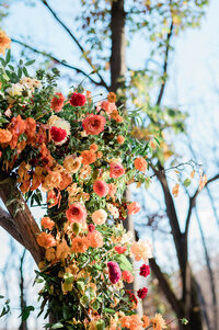 the chuppah’s floral arrangement, showcasing roses, dahlias, and marigolds in shades of orange, red, and yellow