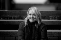 A black and white photo of a blonde woman smiling on a stair set.