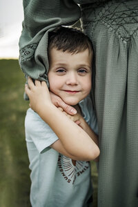 A boy leans into his mom with her hand gently wrapped around whis face