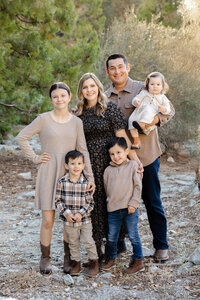 Family of five standing together outdoors in a natural rocky setting with warm neutral outfits, candid family portrait captured by Kaitlyn Dawn Photography, outdoor family photography specialist.