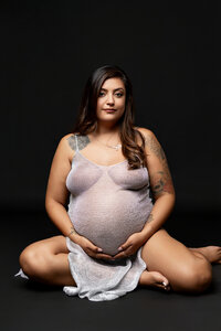 Elegant pregnancy portrait of a pregnant woman sitting on the studio floor wearing a soft textured maternity dress photographed by Kaitlyn Dawn Photography.