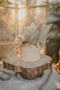 Elegant wedding cake displayed with dried floral accents and decorative reception styling during golden hour.