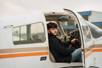Senior portrait at a small hangar near Mobile International Airport in Mobile, Alabama — sitting
in the cockpit with the door open, looking back toward the camera.