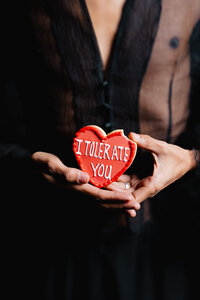 Model photographed against a dark studio backdrop holding a red floral prop.