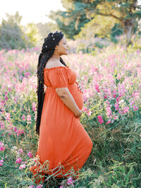 Profile of an expecting mom standing in the blooming sweet pea field, cradling her belly
