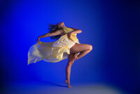 Dancer on pointe in a yellow costume against a vivid blue background, fabric caught mid-motion.