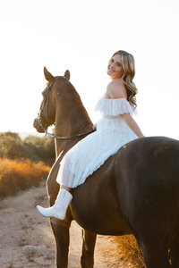 High school senior girl sitting on a horse in a sunlit field during golden hour, Yucaipa outdoor senior portrait by Kaitlyn Dawn Photography.