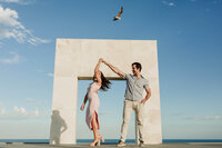 Couple dance beneath a modern seaside arch on a clear blue day