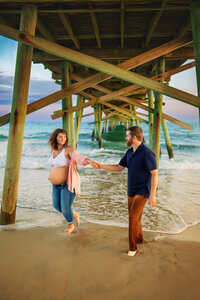 Pregnant couple walking under a pier at the beach during golden hour maternity photography session