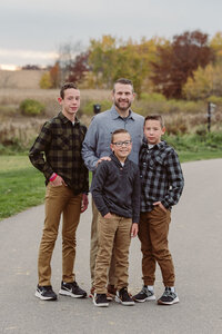 Mother and father with their three sons in coordinated plaid and neutral outfits standing on a path during a Cleveland family photography session