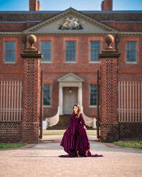 Child in a deep purple gown standing between brick gate pillars at Tryon Palace in New Bern North Carolina