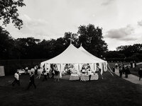 White sailcloth tent set on an open lawn during a summer wedding in Bedford, New York as guests mingle at dusk.
