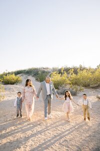 The Collins family walking hand in hand across the Las Vegas desert at golden hour, with parents and three children enjoying a joyful, sunlit outdoor family photography session.