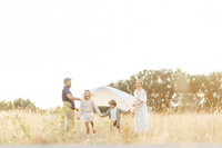 A family standing in a grassy field at a Fort Worth TX park as they play with their children for family photos.