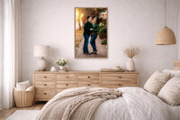 Vertical framed portrait of husband and wife embracing during golden hour in downtown New Bern displayed above dresser in soft neutral bedroom