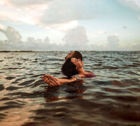 young couple relaxes in water, leaning and embracing with heads tilted towards sky in panama city beach florida