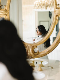 An intentional imagery capture of a bride’s reflection in an ornate gold mirror, showcasing a quiet, natural unfolding of the day.
