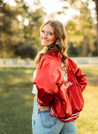 Senior portrait in downtown Magnolia Springs, Alabama — wearing her dance team jacket with hands in her back pockets.