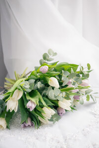 A cream and purple tulip bouquet lay on the lace train of a white wedding dress