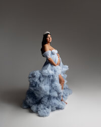 Pregnant woman wearing a flowing blue maternity gown and crown while holding her baby bump during a Yucaipa studio maternity session with Kaitlyn Dawn Photography.