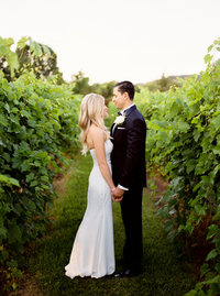 Bride and groom smiling at each other in vineyard