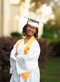 Senior girl posing in her white cap and gown near a school located in downtown Mobile, Alabama.