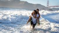 man carrying a woman on his back while running through the high surf at the beach