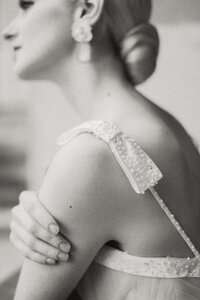 Close-up black and white film-style photograph of a bride's shoulder and pearl-detailed strap, emphasizing a timeless and authentic aesthetic in Paris, France.