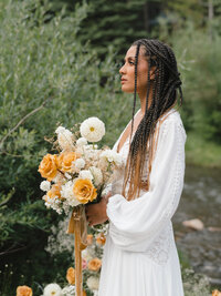 Side profile portrait of bride in a white long sleeve dress holding an orange and white bouquet