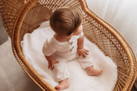 Charleston Baby Milestone Photographer - Baby sits in an antique wicker bassinet during his Milestone Portrait Session at Holy City Babies Portrait Studio in Charleston, SC.