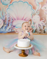 Baby enjoying a cake smash in a pastel mermaid-themed setup. Photograph by Yucaipa cake smash photographer Kaitlyn Dawn Photography.