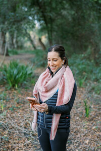 Woman smiling at her phone while taking a walk through the woods